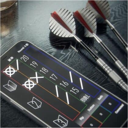 Smartphone screen with a digital dartboard scoring app; three darts lie on a dark table beside it.