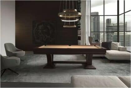 Modern living room with a billiards table, gray chairs, and a sofa near large windows overlooking a city skyline.