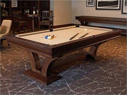 Pool/billiards table set up in a wood-paneled lounge, with balls racked and cues laid out on the felt.