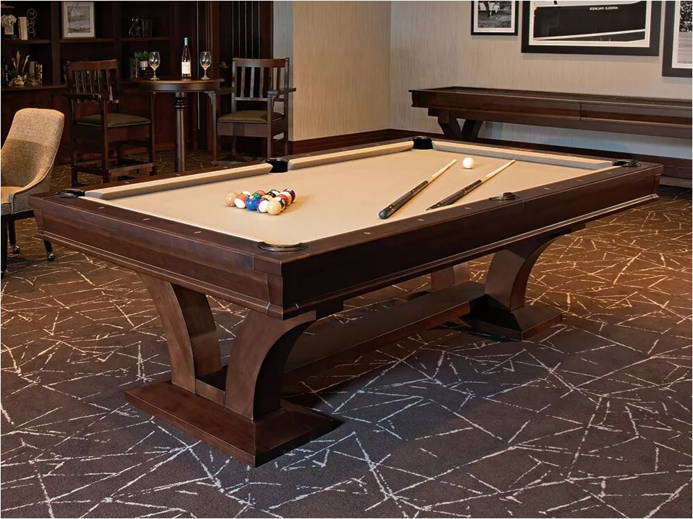 Pool/billiards table set up in a wood-paneled lounge, with balls racked and cues laid out on the felt.