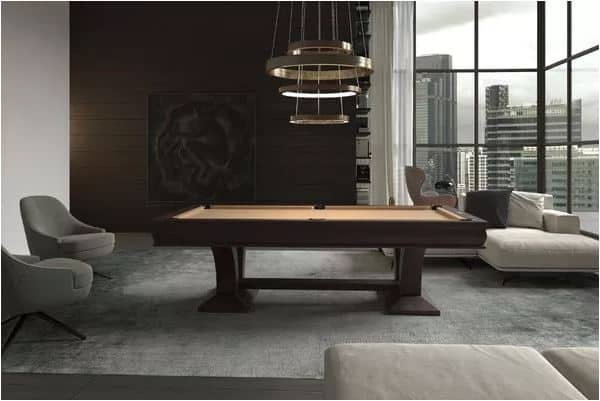 Modern living room with a billiards table, gray chairs, and a sofa near large windows overlooking a city skyline.