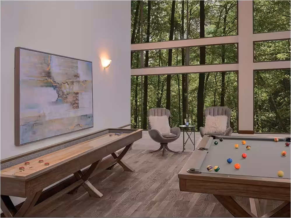 Reagan-Game-room-comp-600x450 | Reagan 7ft or 8ft Billiard Table | West Penn Billiards Luxurious game room with a pool table and a shuffleboard, and floor-to-ceiling forest-view windows behind two cushioned chairs.