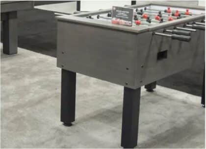 Foosball table on four legs in an indoor game area, with red and black players and a small sign on the playing surface