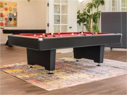 Modern billiards pool table with red felt and scattered balls in a bright living room.