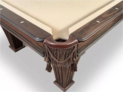 Corner of a dark wood billiards/pool table with a beige felt surface and a tasseled pocket fringe around the pocket edge