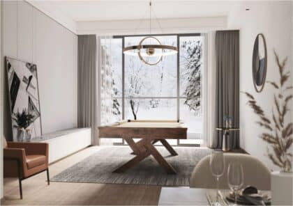 Bright modern living space with a wooden X-legged desk centered on a gray rug, large snowy window behind it and a circular chandelier overhead.