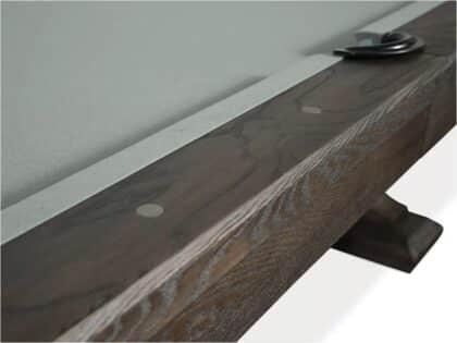 Close-up of a dark wooden shelf edge with a light metal strip and round fasteners, plus a black curved support at the far end.