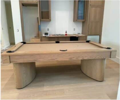 Wood pool table in a room with unfinished kitchen cabinetry and light wood flooring.